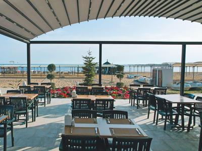 Terrasse eines Restaurants mit Tischen, Stühlen und Blick aufs Meer und den Strand