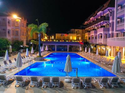 Nachtzicht op een verlicht hotelzwembad met ligstoelen en palmbomen.