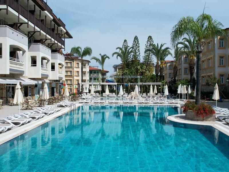 Großer Pool mit Liegestühlen und Palmen in einer Hotelanlage bei klarem Himmel.