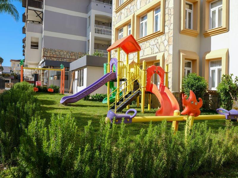 Bunter Kinderspielplatz vor einem Hotelgebäude mit Rutschen und Schaukeln.