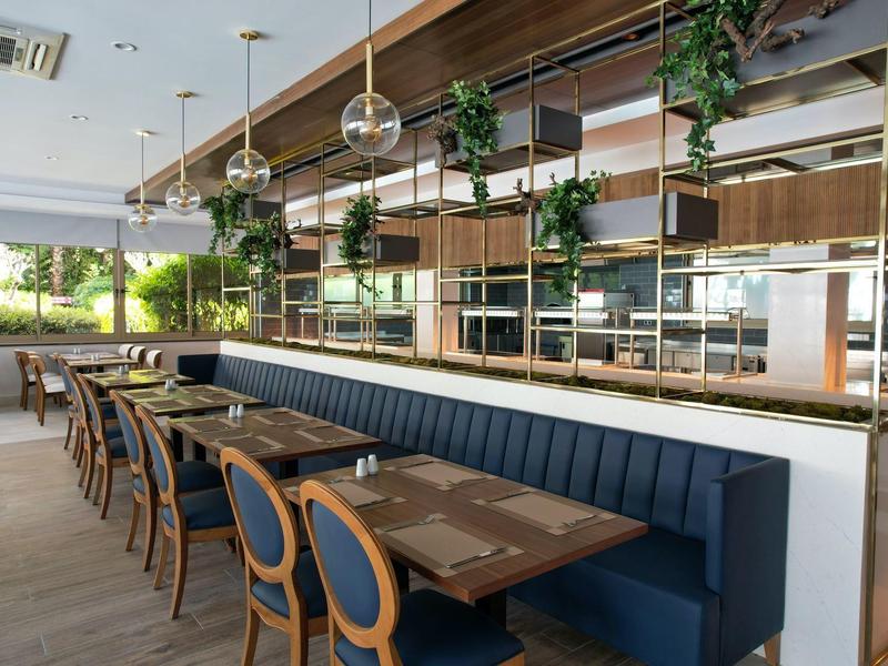 Modern eingerichteter Gastronomiebereich mit blauen Sitzbänken, Holztischen und großen Fenstern.