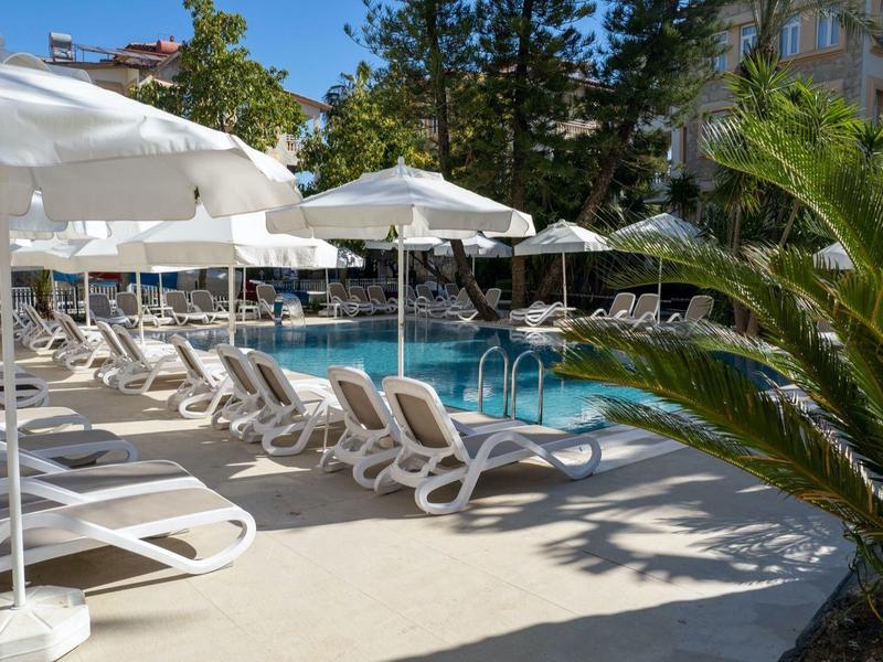 Poolbereich eines Hotels mit weißen Liegestühlen und Sonnenschirmen an einem sonnigen Tag