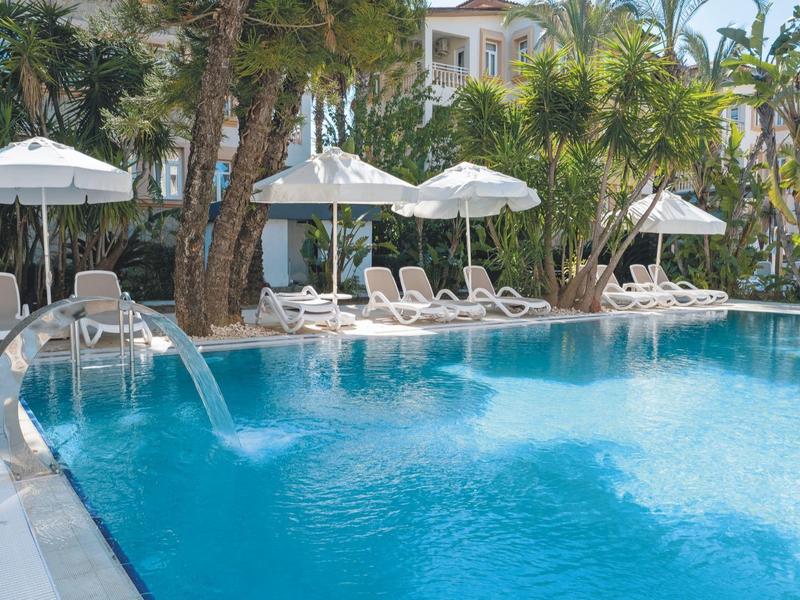 Blauer Hotelpool mit Sonnenliegen, Sonnenschirmen und Palmen im Hintergrund.