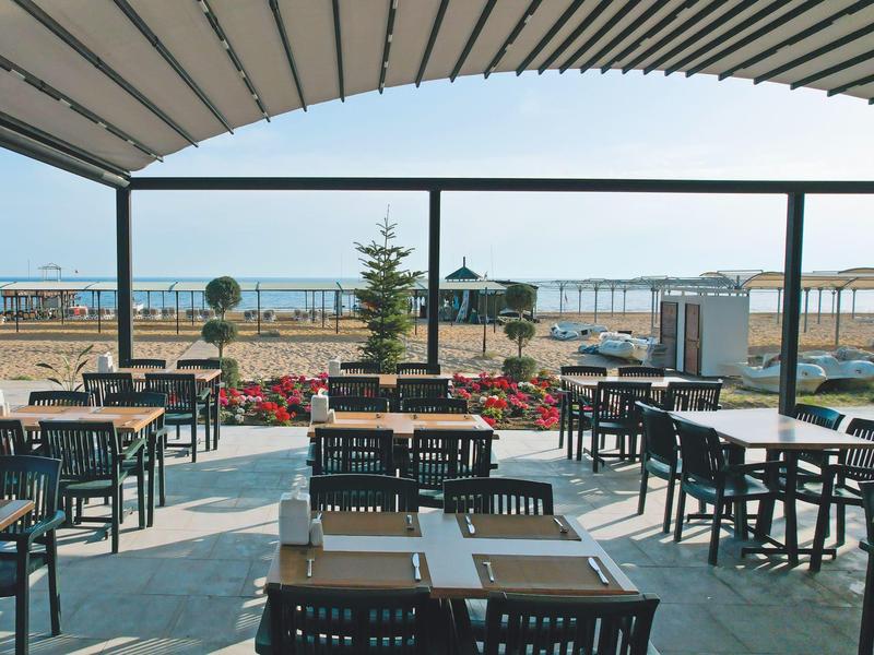 Terrasse eines Restaurants mit Tischen, Stühlen und Blick aufs Meer und den Strand