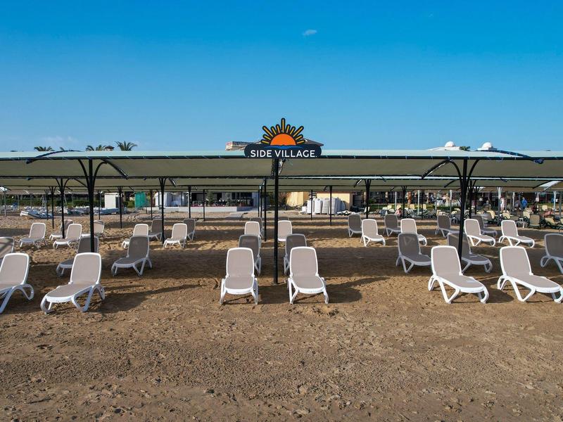 Leere Liegestühle am Strand mit modernen Sonnenschirmen unter blauem Himmel.