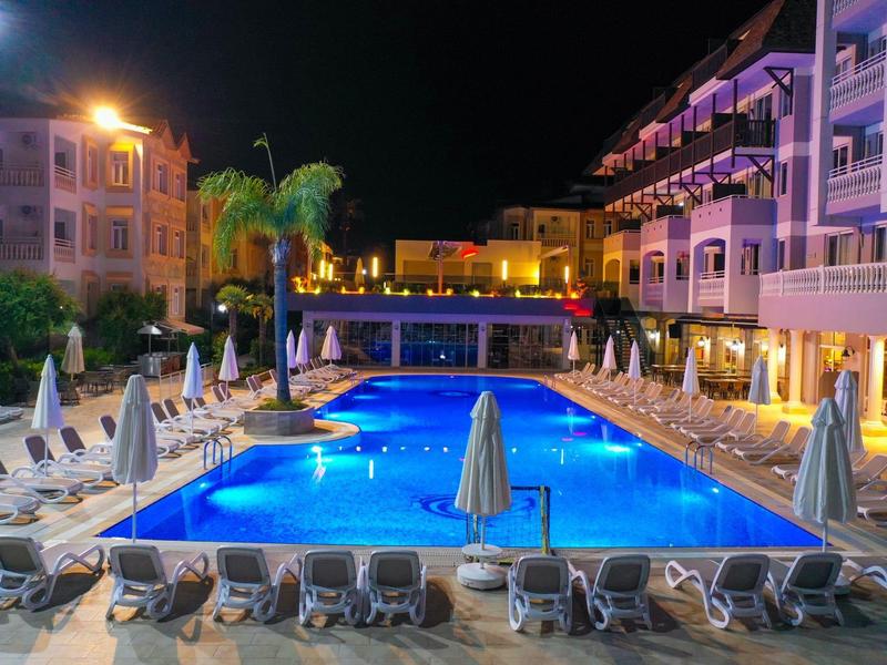 Beleuchteter Poolbereich eines Hotels bei Nacht mit Liegestühlen und Sonnenschirmen.