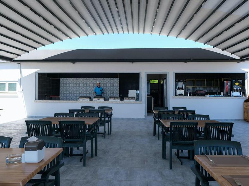 Freiluftrestaurant mit schwarzen Stühlen und Holz-Tischen unter einem hellen, gewölbten Dach.