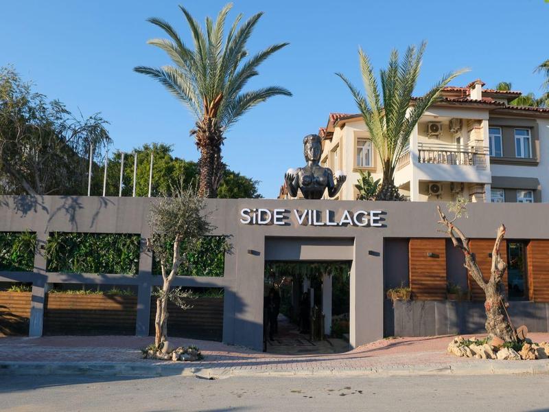 Eingang eines Hotels namens Side Village mit Palmen und Gebäuden im Hintergrund