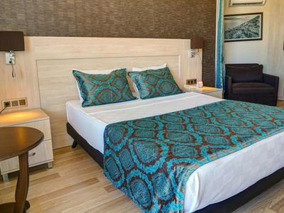 Camera d'hotel moderna con letto grande, comodini e poltrone in toni caldi.