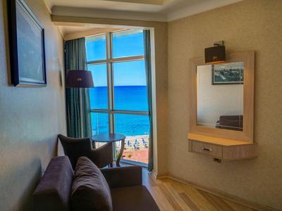 Zimmer mit braunem Sofa, großem Fenster mit Meerblick und Wandspiegel mit Regal.