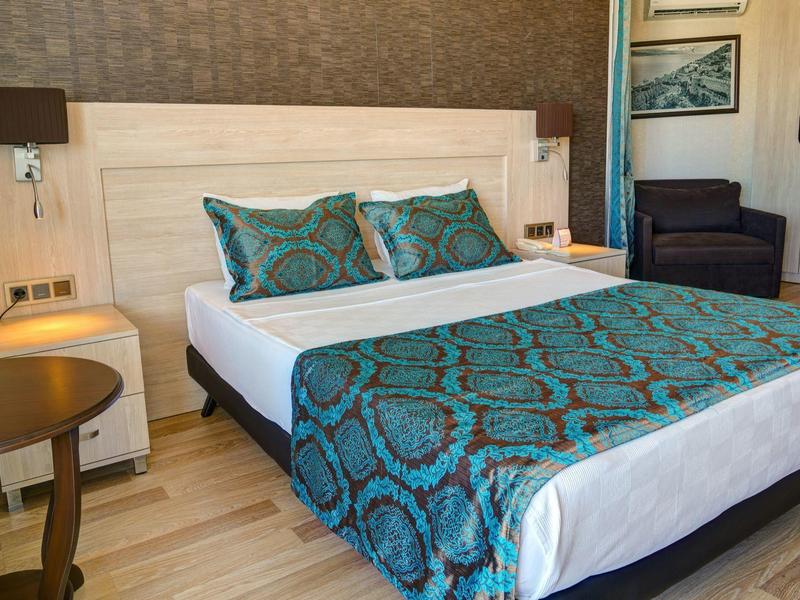 Gemütliches Schlafzimmer mit großem Bett, türkis gemustertem Bettläufer und Nachttischlampen.