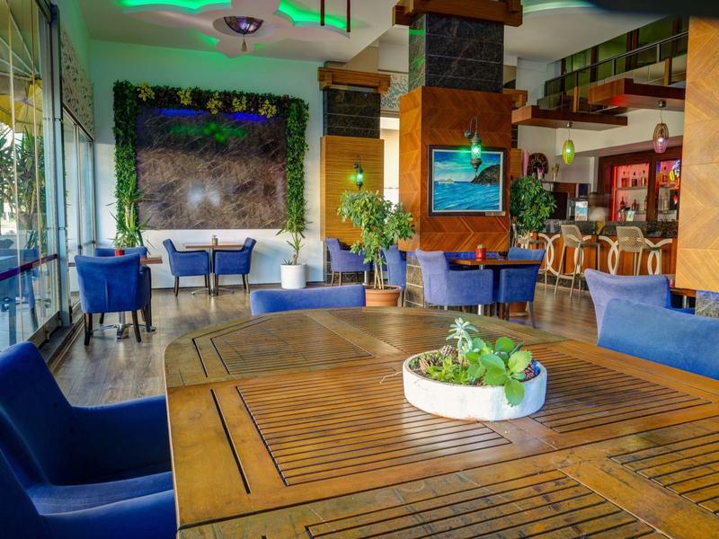 Innenraum eines modernen Restaurants mit Holztischen, blauen Sesseln und großer Fensterfront.