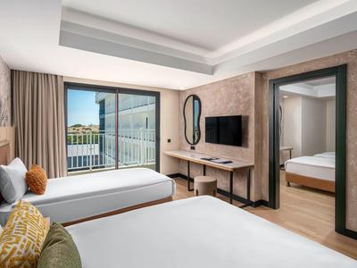 Modernes Hotelzimmer mit zwei Doppelbetten, Schreibtisch, TV und großem Fenster mit Balkonblick.
