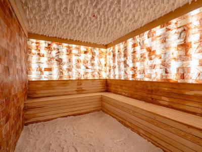 Saunaraum mit holzverkleideten Bänken und Wänden aus leuchtendem Salzstein, Boden mit Salz bedeckt.
