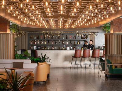 Modern gestaltete Bar mit vielen warmen Deckenleuchten, Sitzgelegenheiten und Pflanzen.
