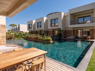 Modern hotelzwembad met houten terras en meerlaagse kamers in een zonnige omgeving.