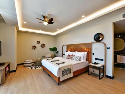 Modern hotelkamer met kingsize bed, plafondventilator en warme houten vloer.