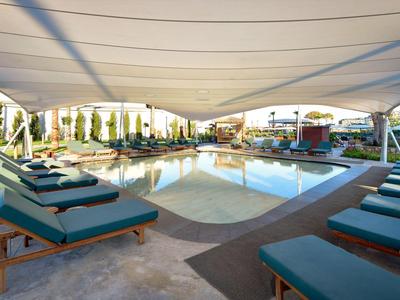 Moderne buitenzwembad met ligstoelen en groot zonnescherm in een hotelomgeving