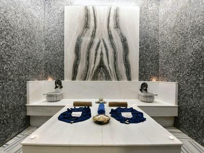 Moderní wellness místnost se dvěma masážními stoly a monochromatickým dekorativním designem na stěně.