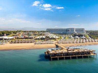 Pohled na pláž s lehátky, slunečníky a molem před velkým hotelem za jasné oblohy.