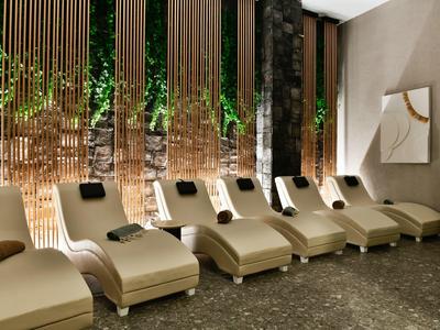 Šest pohodlných lehátek ve stylové wellness oblasti s visícími rostlinami a dekorativními závěsy.