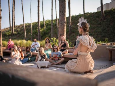 Vrouw mediteert buiten voor een groep mensen in een ontspannen sfeer.