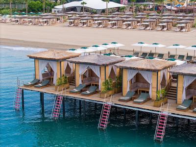 Bungalovy na molu nad čistou vodou s lehátky a slunečníky na pláži.