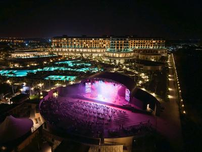 Luxe hotel 's nachts met verlichte zwembad en buitenpodium.