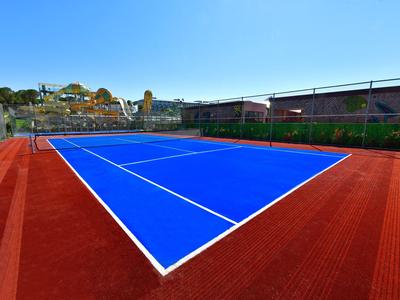 Een tennisbaan met een blauw speelveld en een rode ondergrond onder een heldere lucht.