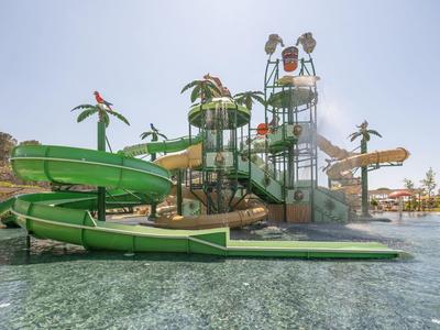 Vodní park se zelenými tobogány, palmami a bazény pod jasnou oblohou.