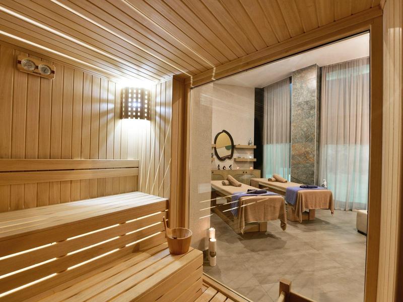 Útulná dřevěná sauna s výhledem na wellness prostor s masážními lehátky.