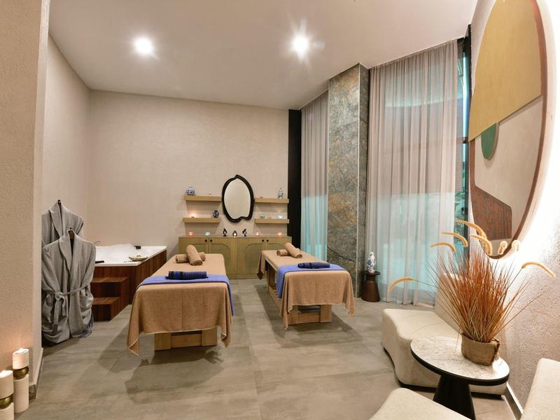 Světlá masážní místnost se dvěma lehátky, kulatým zrcadlem a tlumeným osvětlením.
