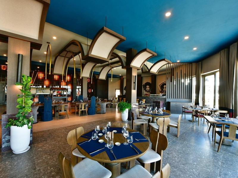 Moderní restaurace s modrým stropem, dřevěným nábytkem a velkými okny