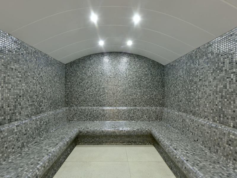 Moderní parní místnost se šedými mozaikovými dlaždicemi a integrovaným osvětlením.