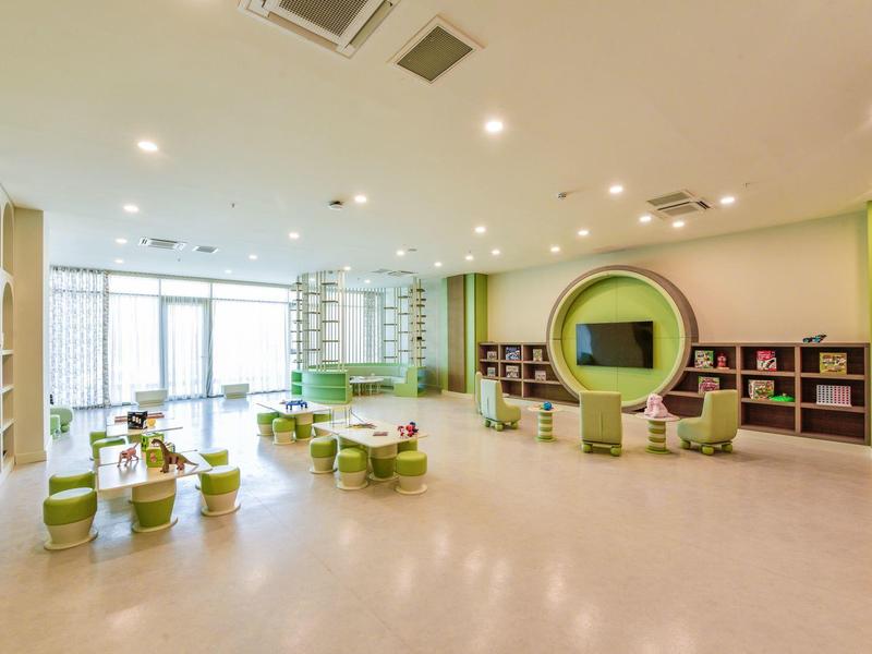 Světlá dětská zóna s moderním nábytkem, hracími stoly a knihovnami v hotelu.