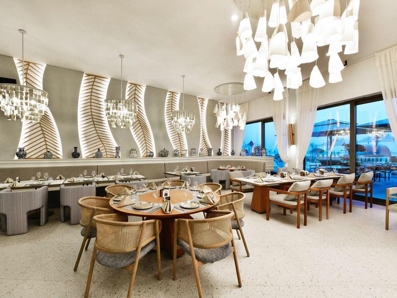 Moderní restaurace s kulatými dřevěnými stoly, pohodlnými židlemi a velkým oknem s výhledem ven.