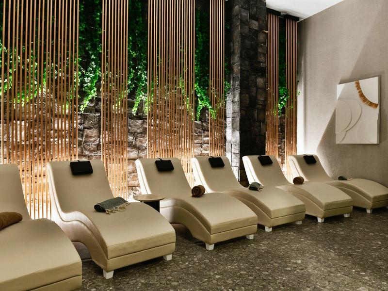Šest pohodlných lehátek ve stylové wellness oblasti s visícími rostlinami a dekorativními závěsy.