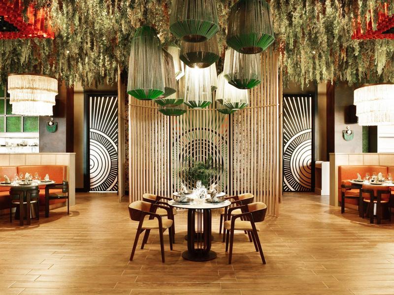 Elegantní restaurace s dřevěným interiérem a zelenými závěsnými rostlinami na stropě.