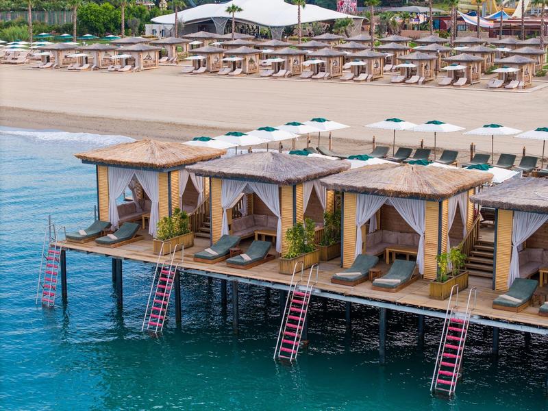 Bungalovy na molu nad čistou vodou s lehátky a slunečníky na pláži.