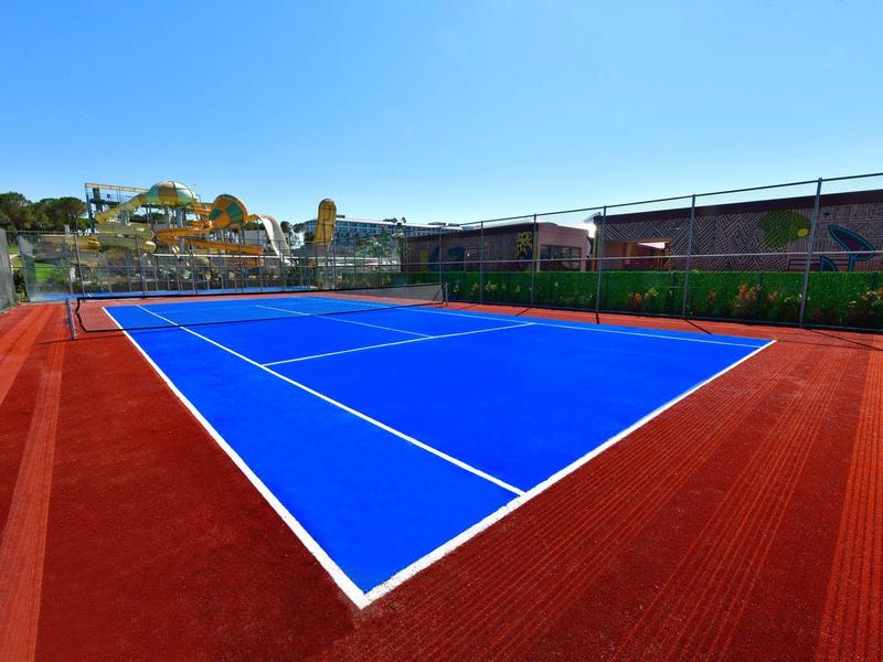 Modrý tenisový kurt s červeným povrchem a jasnou oblohou v pozadí.