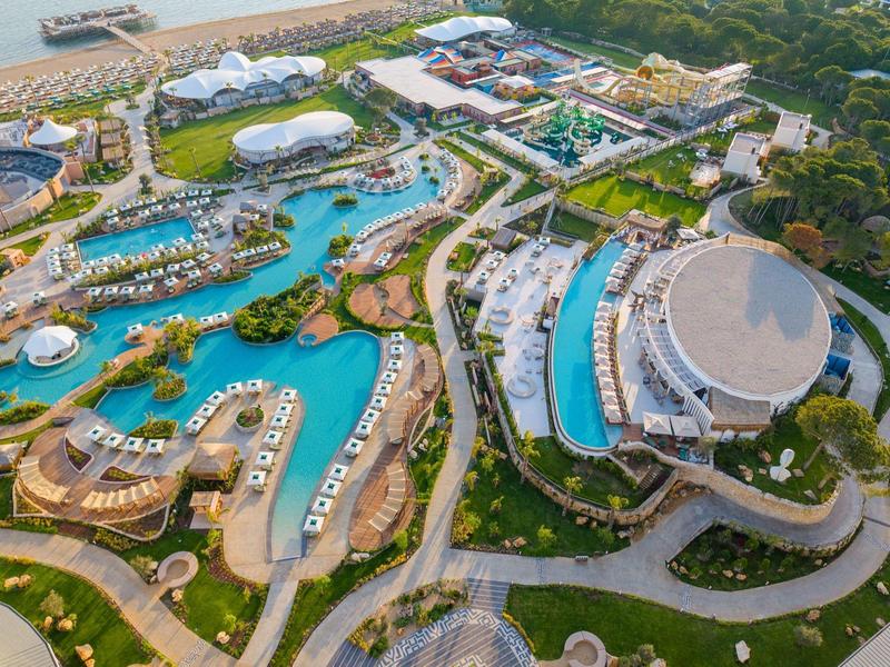 Letecký pohled na velký resort s několika bazény, odpočinkovými oblastmi a obklopený zelení.
