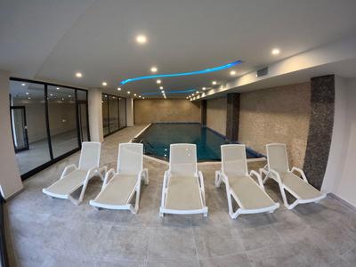 Vnitřní bazén s lehátky a nepřímým modrým osvětlením stropu v moderní místnosti.