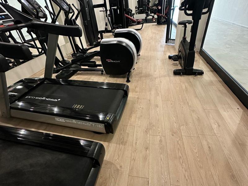 Moderní posilovna s běžeckými pásy, rotopedy a závažími na dřevěné podlaze.