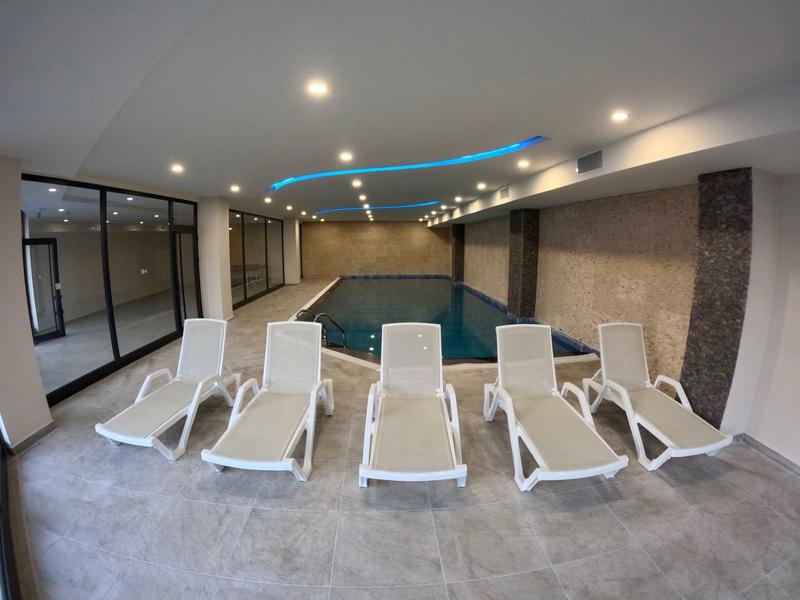 Vnitřní bazén s šesti bílými lehátky a moderním stropním osvětlením.