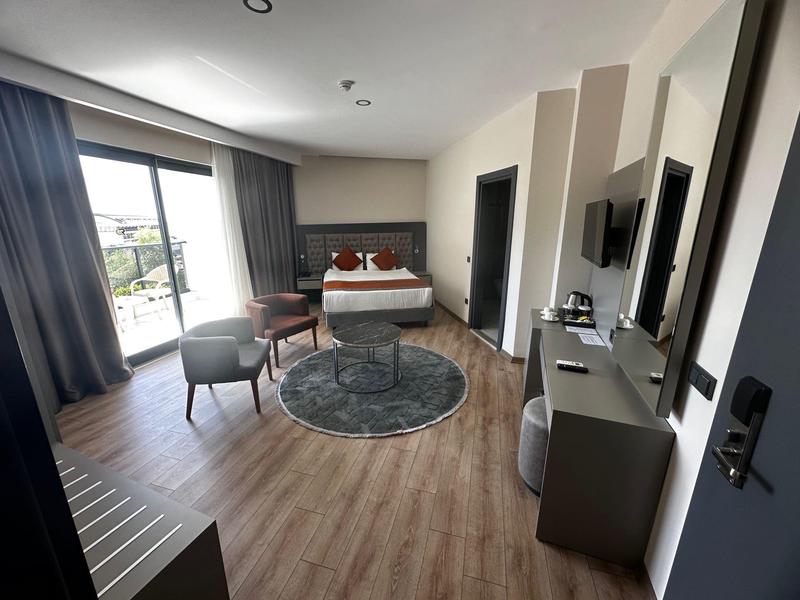 Moderní hotelový pokoj s manželskou postelí, posezením, malým kobercem a balkonem s výhledem.