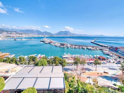 View of a harbor with boats, a promenade, and mountains in the background under clear sky.