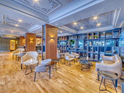 Zona de lounge moderna en hotel con sillas claras, mesas y estanterías decorativas.