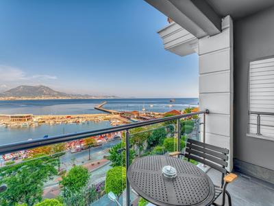 Balcón con mesa y sillas con vista al puerto y montañas bajo cielo despejado.