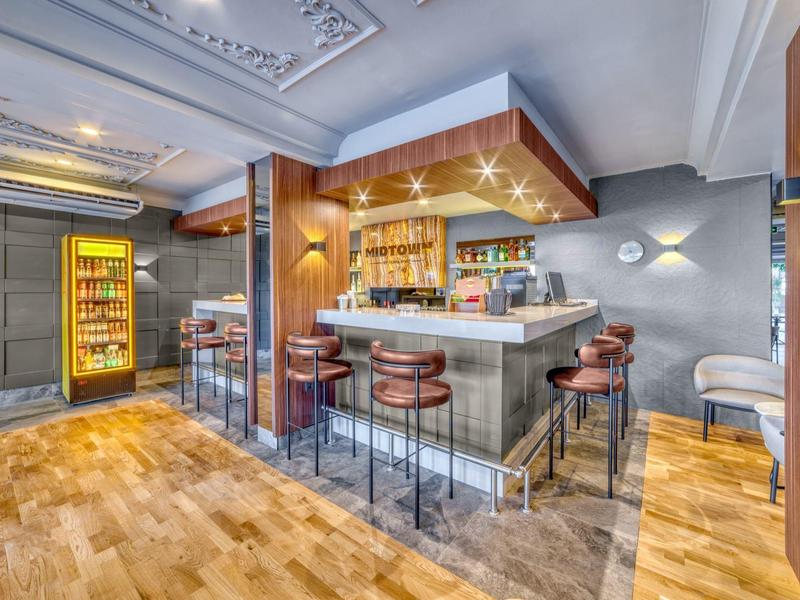 Modern hotel bar area with wooden flooring, seating, and illuminated refrigerator.