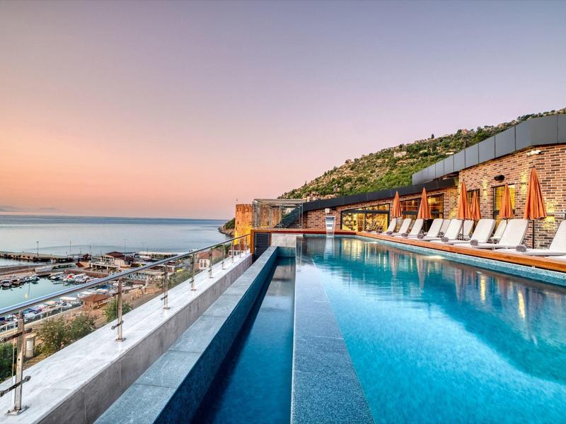 Infinity pool with sun loungers overlooking the sea and coastline at sunset.